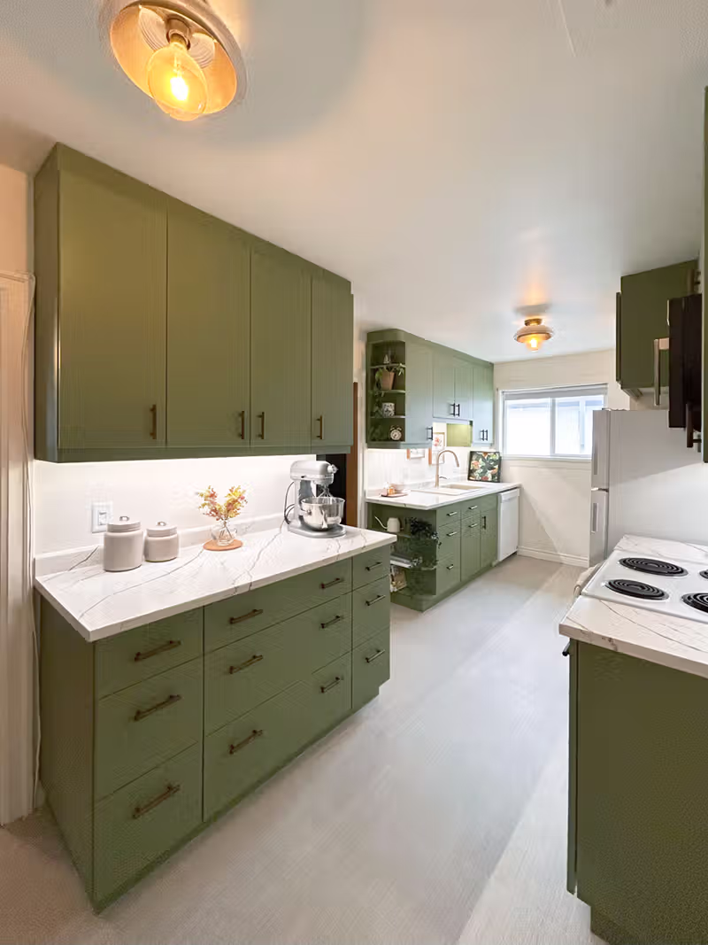 Full-length view of the renovated Ferry Road galley kitchen with olive green cabinets on both sides and white appliances.