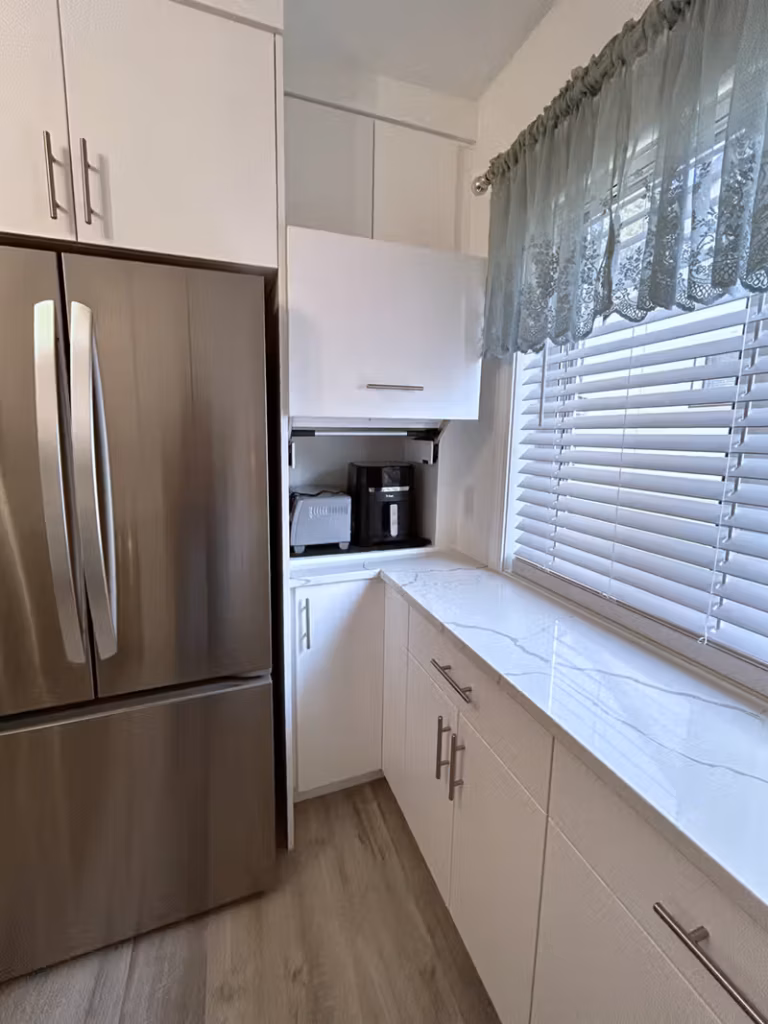 Kitchen counter with a stainless steel French door refrigerator, white cabinets, and quartz countertops near a window