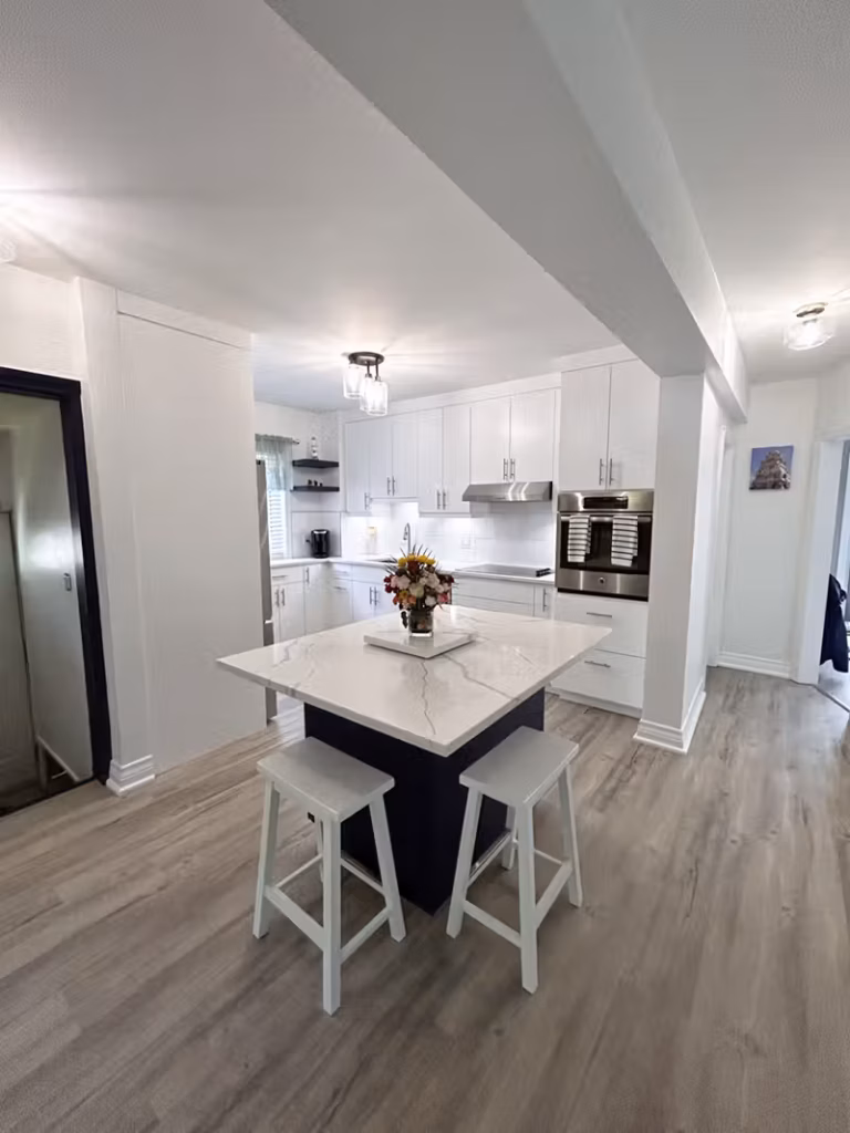 Navy blue kitchen island with a white quartz countertop and white bar stools in an open white kitchen