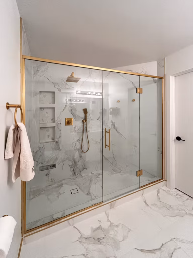 Renovated bathroom with a large marble-tiled glass shower, brushed gold fixtures, and matching tile flooring